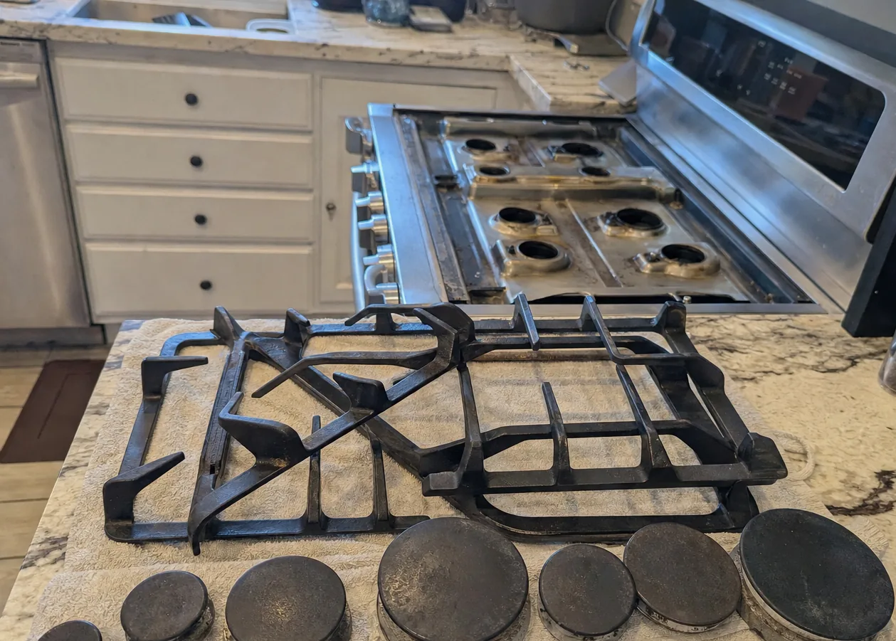 A cooking surface stripped for service in a kitchen, the grates stacked on the counter and the burner bases uncovered below the hood line